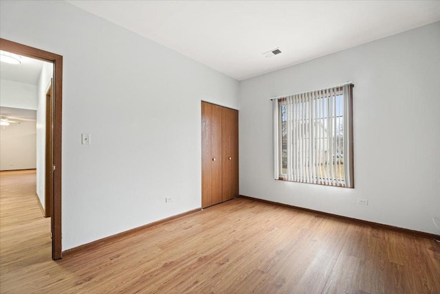 unfurnished bedroom featuring light wood finished floors, baseboards, visible vents, and a closet