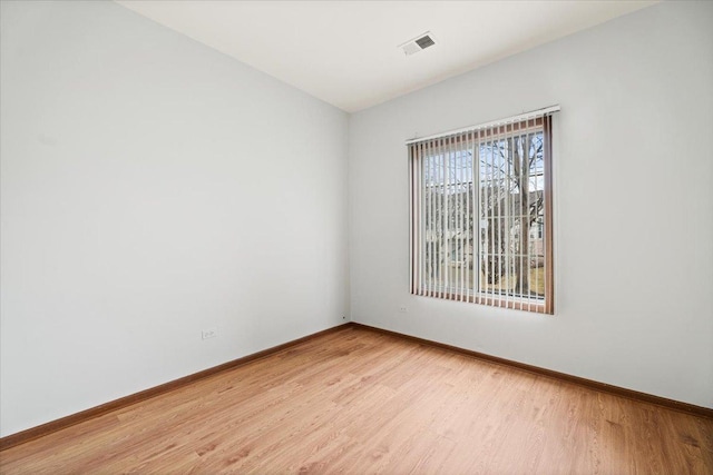 empty room with light wood finished floors, visible vents, and baseboards