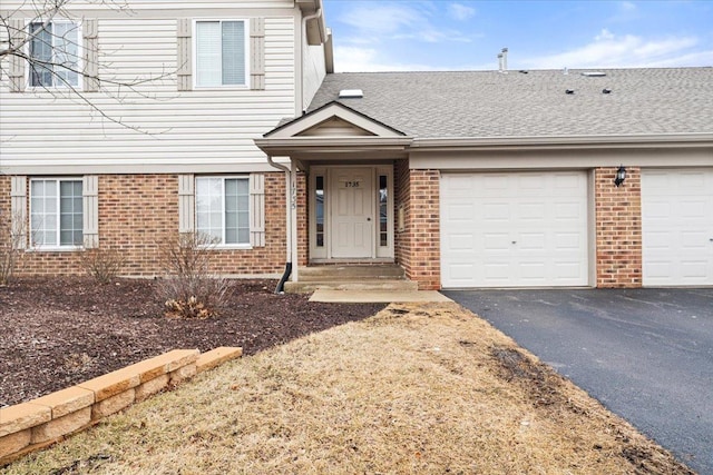 traditional-style home featuring an attached garage, aphalt driveway, a shingled roof, and brick siding