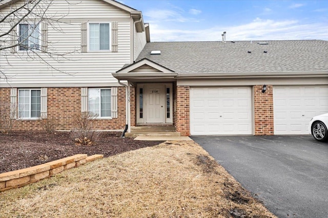 view of front facade with driveway, roof with shingles, an attached garage, and brick siding