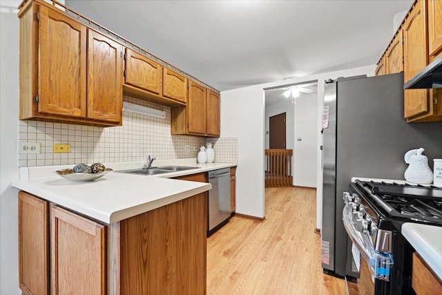 kitchen with stainless steel appliances, a sink, light countertops, decorative backsplash, and light wood finished floors