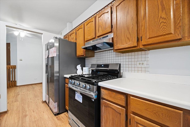 kitchen with brown cabinets, light countertops, backsplash, appliances with stainless steel finishes, and under cabinet range hood