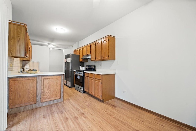 kitchen featuring light wood-style flooring, under cabinet range hood, black fridge with ice dispenser, light countertops, and stainless steel range with gas cooktop