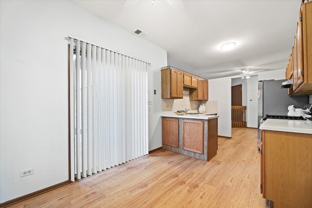 kitchen featuring ceiling fan, light wood-style flooring, light countertops, backsplash, and brown cabinets