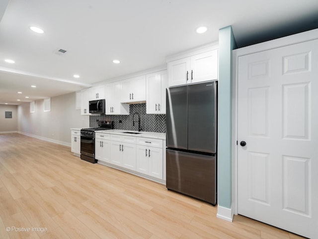 kitchen featuring white cabinetry, stainless steel refrigerator, black range with gas stovetop, light hardwood / wood-style flooring, and sink