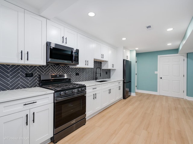 kitchen with range with gas cooktop, white cabinetry, backsplash, black fridge, and light wood-type flooring