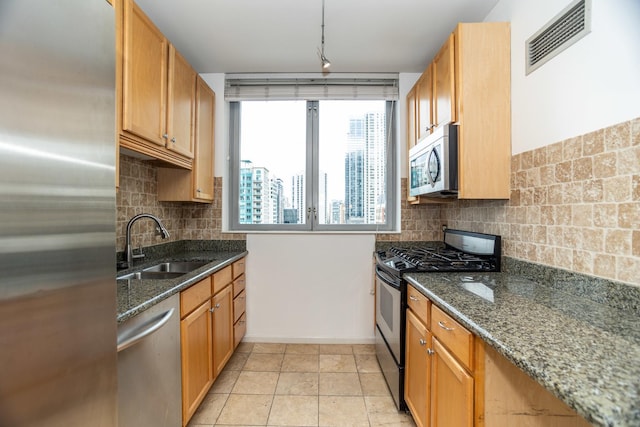 kitchen with light tile patterned floors, sink, appliances with stainless steel finishes, and dark stone countertops