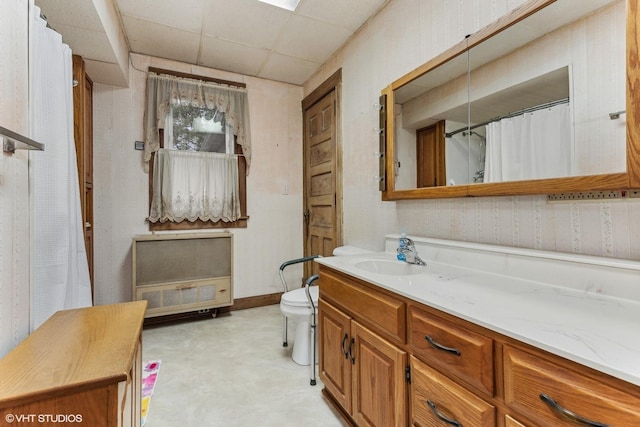 bathroom featuring toilet, heating unit, vanity, and a paneled ceiling