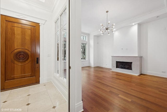 entrance foyer with light wood finished floors, baseboards, a premium fireplace, crown molding, and a notable chandelier