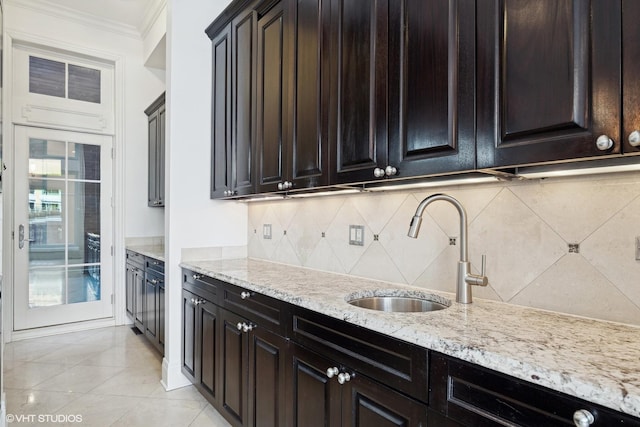 kitchen with light stone counters, light tile patterned floors, tasteful backsplash, ornamental molding, and a sink