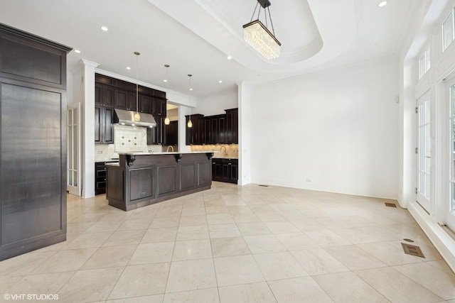 kitchen with light countertops, pendant lighting, a kitchen island with sink, and under cabinet range hood