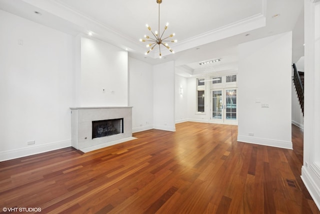 unfurnished living room with baseboards, a fireplace with flush hearth, wood finished floors, a tray ceiling, and crown molding