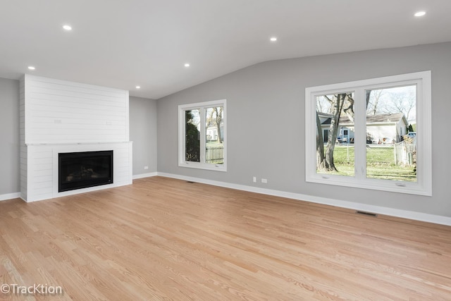 unfurnished living room featuring vaulted ceiling, a large fireplace, a healthy amount of sunlight, and light hardwood / wood-style floors