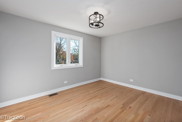 unfurnished room featuring an inviting chandelier and light hardwood / wood-style flooring