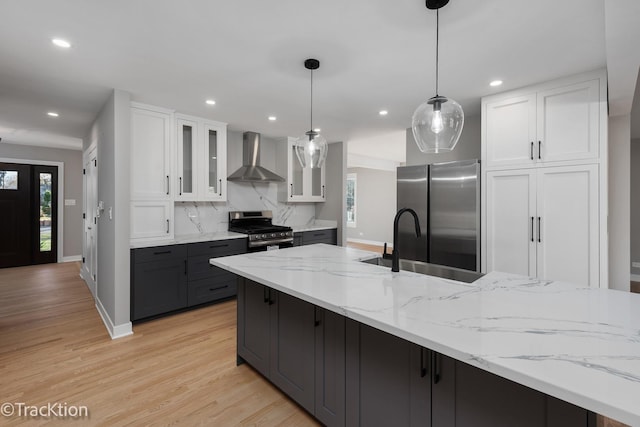 kitchen featuring white cabinets, decorative light fixtures, wall chimney range hood, stainless steel appliances, and decorative backsplash