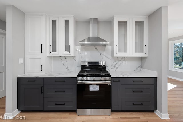 kitchen featuring wall chimney exhaust hood, gas stove, white cabinetry, and light hardwood / wood-style floors