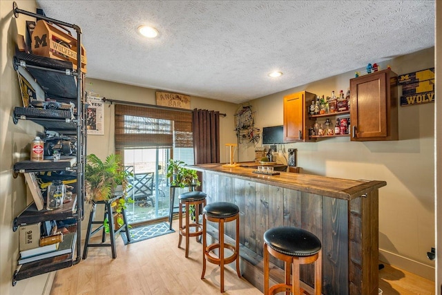 bar with a textured ceiling, light hardwood / wood-style flooring, and wooden counters