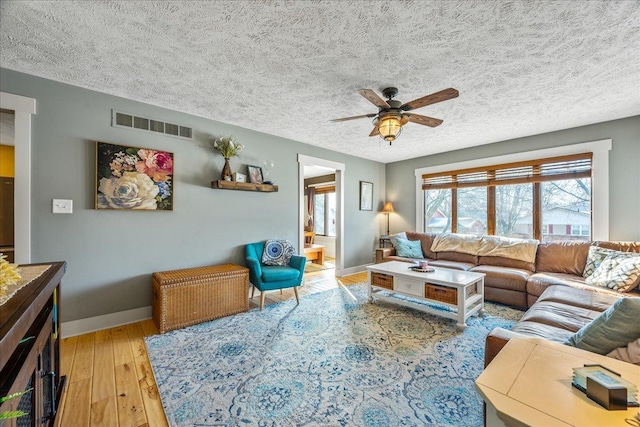 living room featuring ceiling fan, light hardwood / wood-style floors, and a textured ceiling