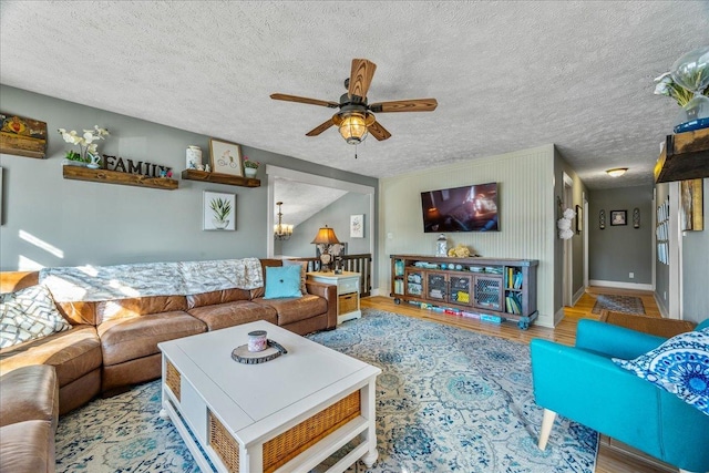 living room with ceiling fan with notable chandelier, a textured ceiling, and light hardwood / wood-style flooring