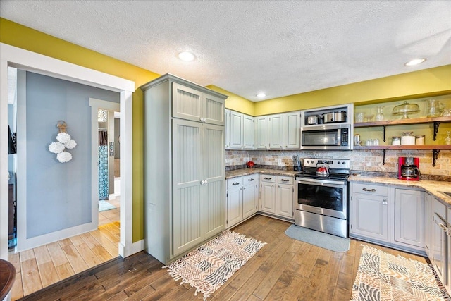 kitchen with stainless steel appliances, a textured ceiling, decorative backsplash, and wood-type flooring