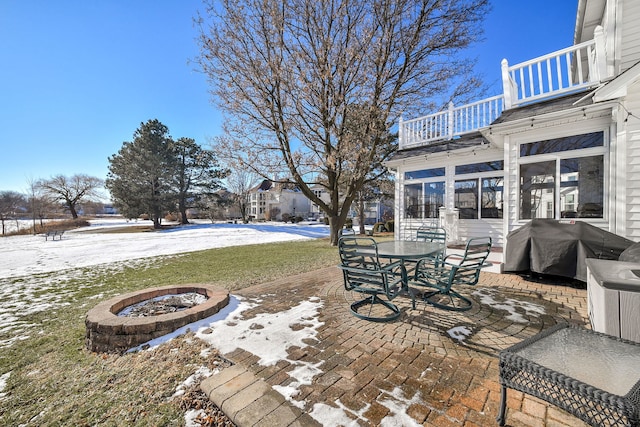 snow covered patio featuring a balcony, a sunroom, grilling area, and an outdoor fire pit