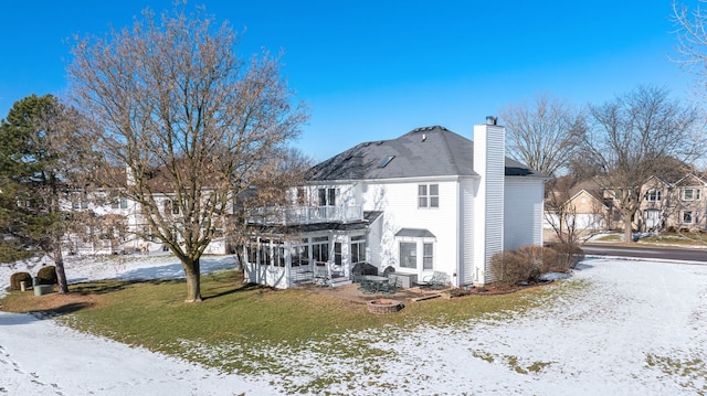 snow covered house featuring a lawn and a balcony