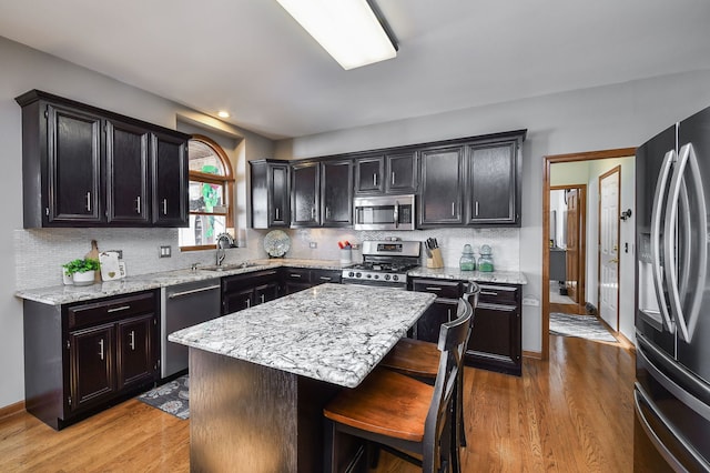 kitchen with sink, a kitchen island, stainless steel appliances, a kitchen bar, and light wood-type flooring