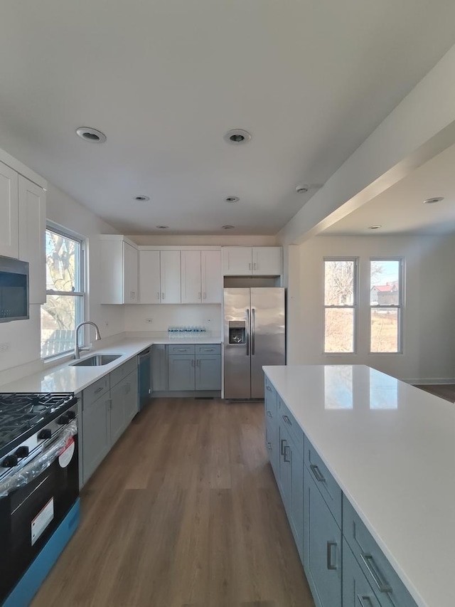 kitchen with a sink, wood finished floors, white cabinetry, stainless steel appliances, and light countertops