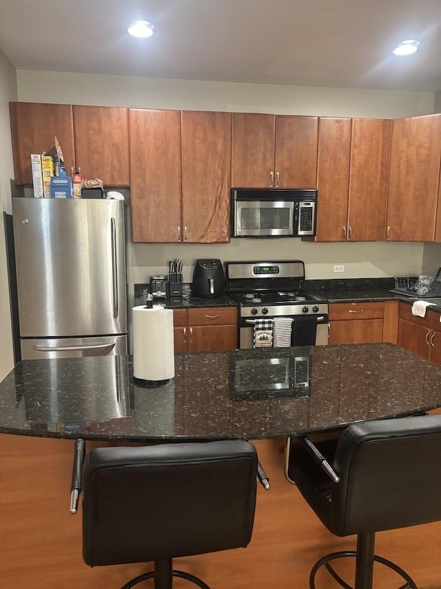 kitchen with appliances with stainless steel finishes, a kitchen bar, a center island, and dark stone countertops