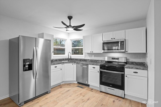 kitchen with white cabinets, appliances with stainless steel finishes, tasteful backsplash, sink, and light hardwood / wood-style flooring