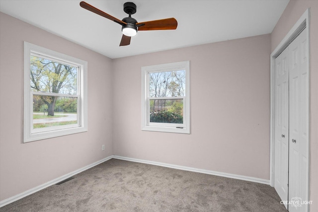 unfurnished bedroom featuring ceiling fan, a closet, light colored carpet, and multiple windows