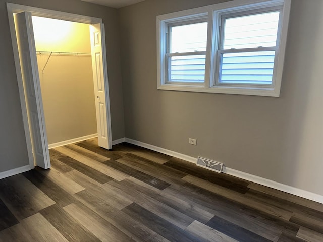 unfurnished bedroom featuring a spacious closet, dark wood-type flooring, and a closet