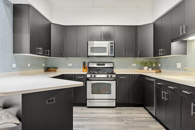 kitchen featuring sink, tasteful backsplash, kitchen peninsula, stainless steel appliances, and light hardwood / wood-style floors