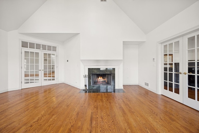 unfurnished living room with hardwood / wood-style floors, a fireplace, high vaulted ceiling, and french doors