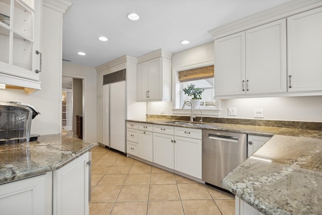 kitchen with sink, light tile patterned floors, stainless steel dishwasher, stone counters, and white cabinets