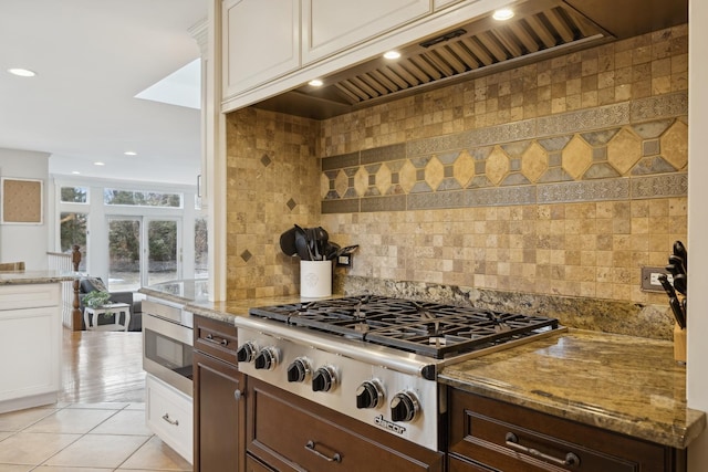 kitchen featuring custom exhaust hood, white cabinetry, light tile patterned floors, stainless steel appliances, and light stone countertops