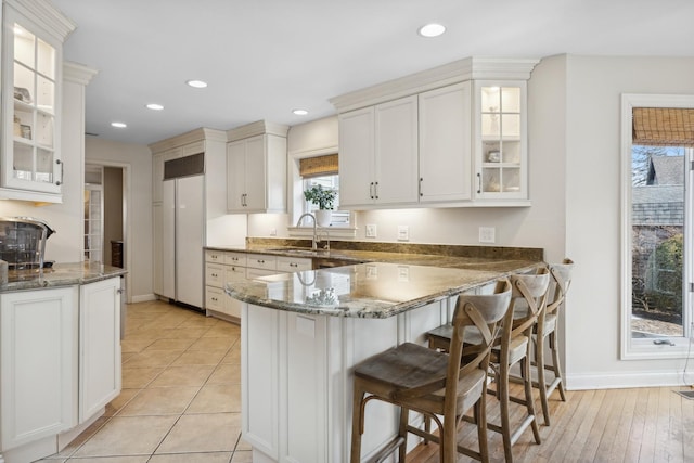 kitchen featuring dark stone countertops, sink, kitchen peninsula, and white cabinets