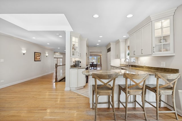 kitchen with sink, stone counters, white cabinetry, kitchen peninsula, and light wood-type flooring