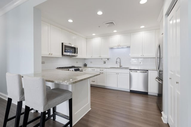 kitchen with sink, stainless steel appliances, white cabinets, a kitchen bar, and kitchen peninsula