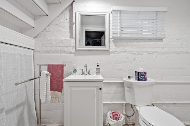 bathroom with brick wall, toilet, and vanity