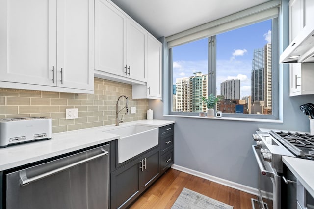 kitchen featuring wood-type flooring, sink, white cabinetry, stainless steel appliances, and wall chimney exhaust hood