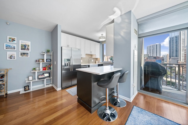 kitchen featuring stainless steel fridge with ice dispenser, white cabinetry, light hardwood / wood-style floors, backsplash, and sink