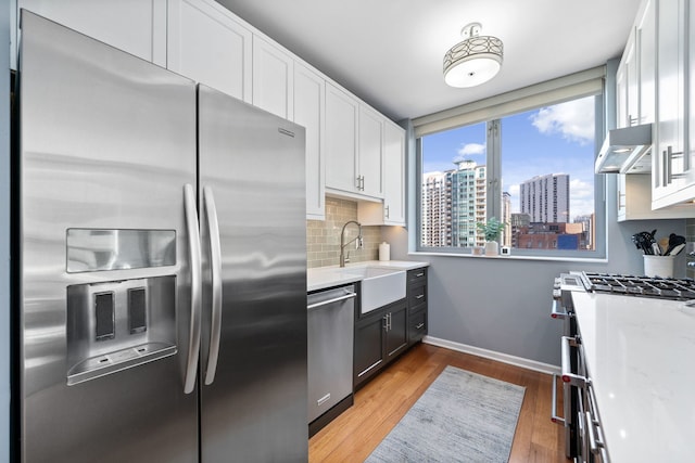 kitchen featuring range hood, wood-type flooring, sink, appliances with stainless steel finishes, and white cabinets