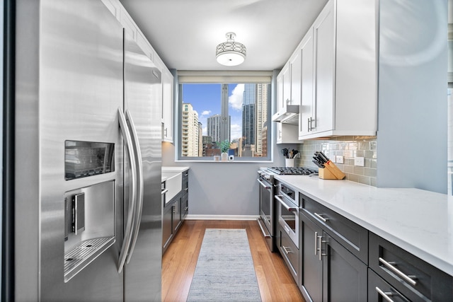 kitchen with white cabinetry, light hardwood / wood-style floors, appliances with stainless steel finishes, decorative backsplash, and light stone countertops