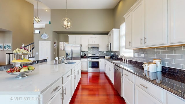 kitchen featuring appliances with stainless steel finishes, white cabinets, sink, hanging light fixtures, and a kitchen island with sink