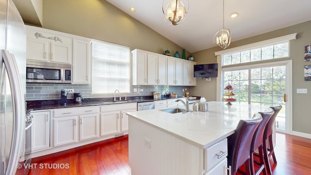 kitchen featuring appliances with stainless steel finishes, decorative light fixtures, sink, a kitchen island with sink, and vaulted ceiling