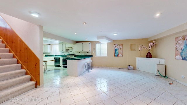 kitchen with light tile patterned floors, kitchen peninsula, stainless steel range, black dishwasher, and a breakfast bar