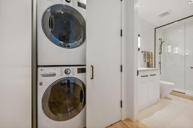 laundry area with stacked washer / drying machine and light wood-type flooring