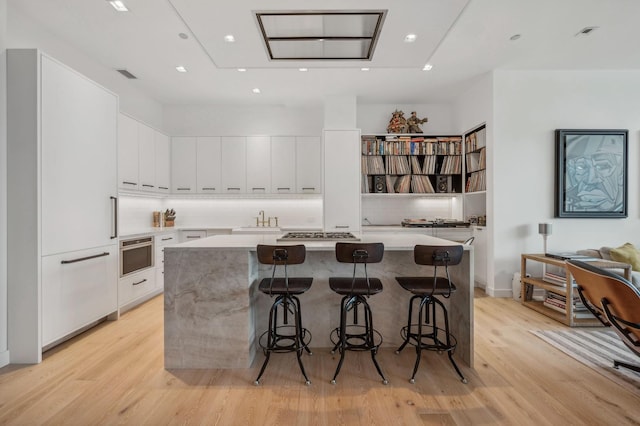 kitchen with white cabinets, appliances with stainless steel finishes, a kitchen island, light wood-type flooring, and a breakfast bar