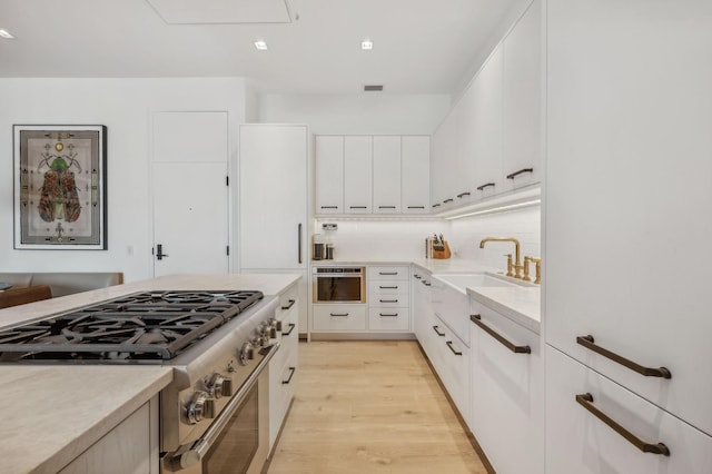 kitchen with sink, white cabinets, light wood-type flooring, and stainless steel gas range oven